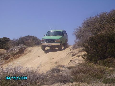 1990 Ford Bronco - 1990 Ford Bronco navigating an off-road trail on a sunny day.