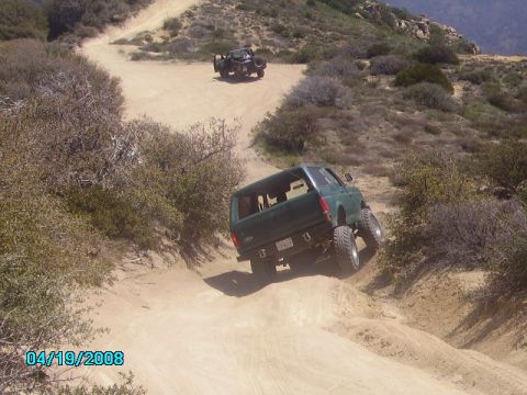 1990 Ford Bronco - Two off-road vehicles navigate a challenging dirt path on a sunny day.