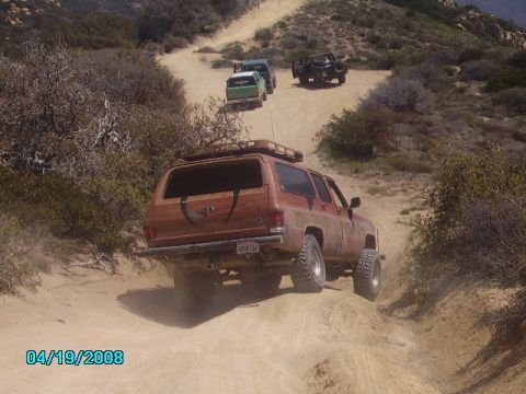 1990 Ford Bronco - Several off-road vehicles navigate a steep, dusty trail in a , natural landscape.