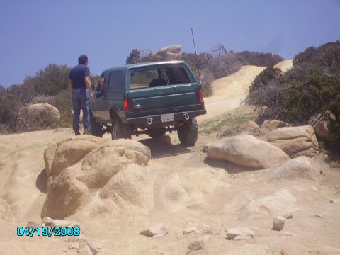 1990 Ford Bronco - A green 1990 Ford Bronco navigates a challenging off-road course on a sunny day.