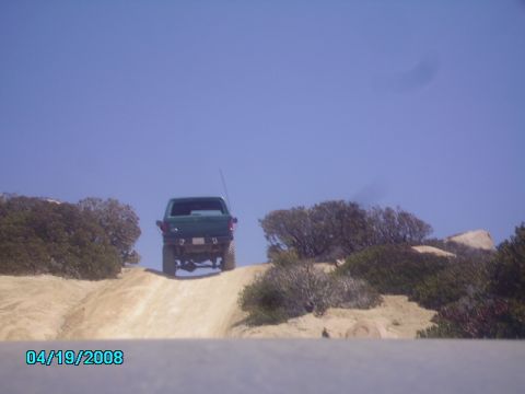 1990 Ford Bronco - A green pickup truck ascends a dusty incline under a clear blue sky.