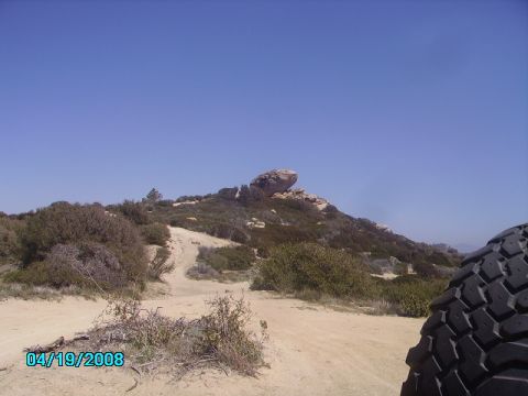 1990 Ford Bronco - A scenic view of a rocky hill and a dirt path, with a tire visible in the foreground.
