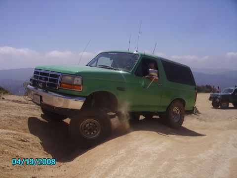 1990 Ford Bronco - This green Ford Bronco is navigating a dusty off-road trail with another vehicle behind it.