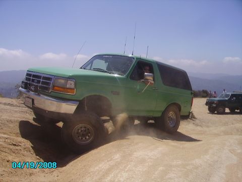 1990 Ford Bronco - A green Ford Bronco navigates a dusty off-road trail with another vehicle in the background.