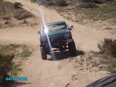1990 Ford Bronco - Green 1990 Ford Bronco navigates an off-road trail, showing its lifted suspension and tires.
