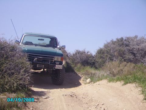 1990 Ford Bronco - This green Ford F-Series truck, likely a 1987 model, navigates a dusty, off-road trail.