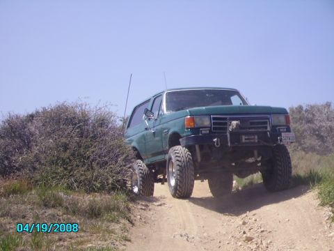 1990 Ford Bronco - Ford Bronco navigates an off-road trail under a clear blue sky.