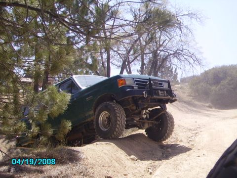 1990 Ford Bronco - A green Ford Bronco navigates a dusty, off-road trail with its front-left tire lifted.