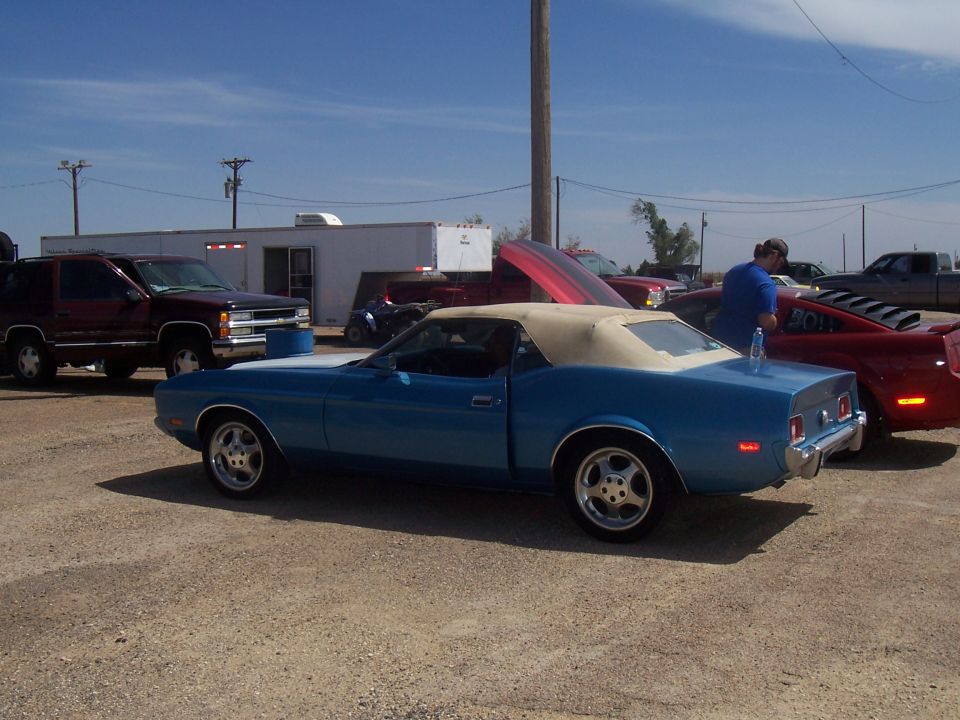Blue convertible car with a tan top, seen from the rear quarter angle. Chrome wheels and bumper are visible