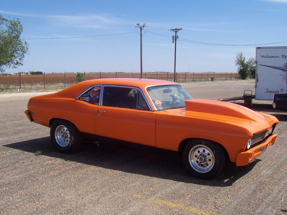 Orange drag car with a large hood scoop and racing decals on the window