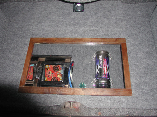Wood-framed glass display box in trunk holding a car amplifier and Acoustik capacitor