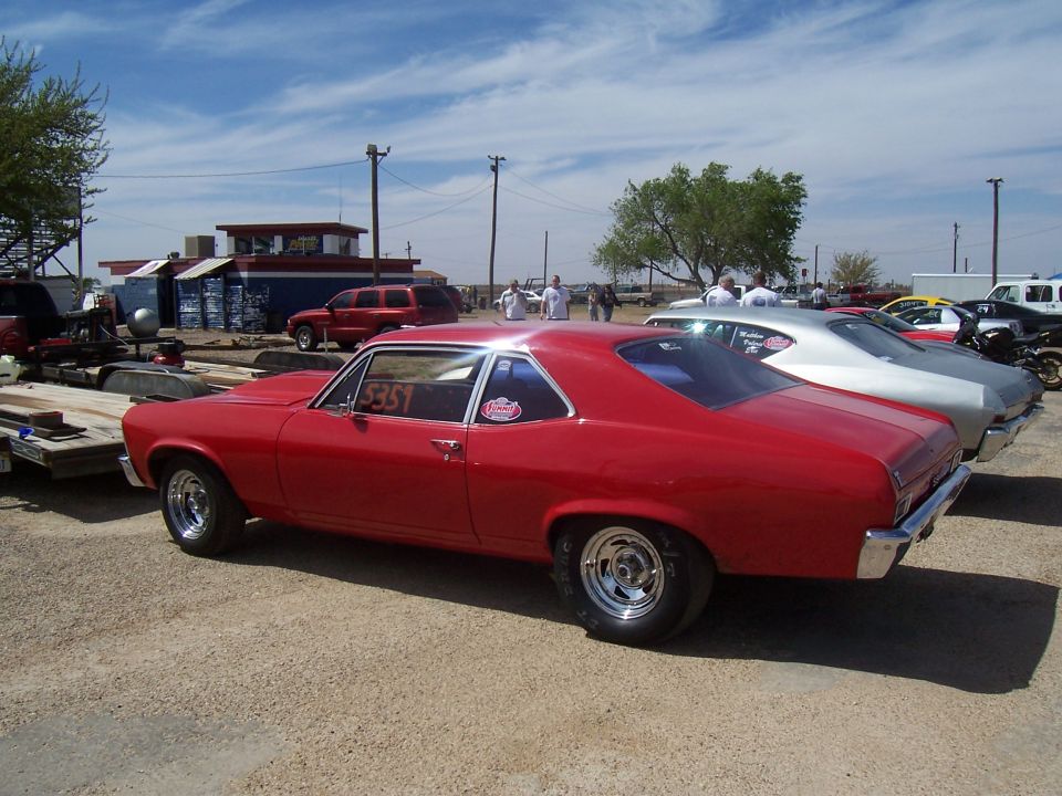 Red coupe with racing slicks and a "351" sticker on the window, parked at a drag strip