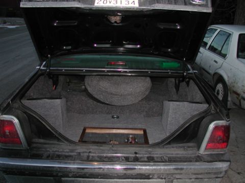 1988 Ford LTD Crown Victoria - Open trunk of a dark full-size sedan showing a custom gray-carpeted audio install: molded corner enclosures on both sides, a raised carpete…