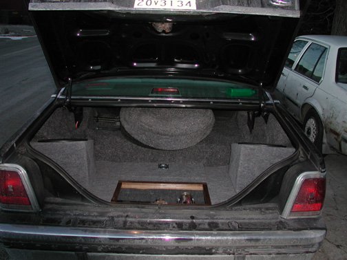 Sedan trunk with custom gray-carpeted subwoofer enclosures and amplifier wiring panel