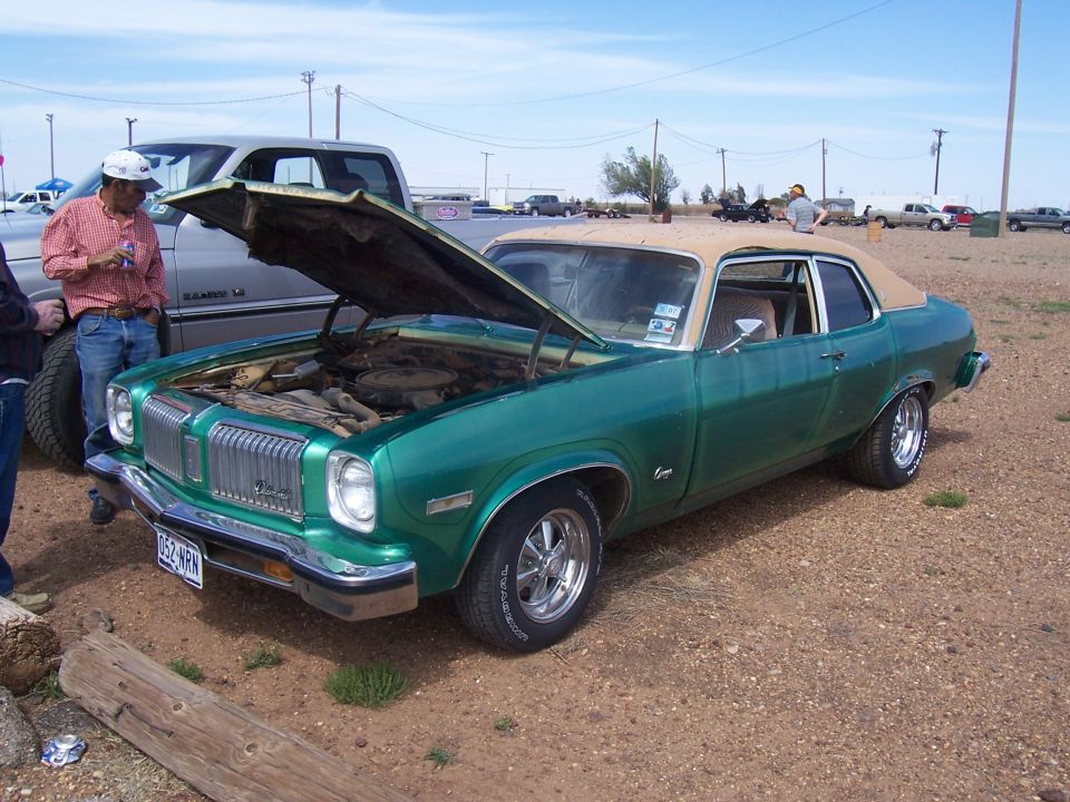 Green coupe with tan roof, hood open, showing engine. Chrome grille and bumpers. Aftermarket wheels. License plate reads 052-NRN