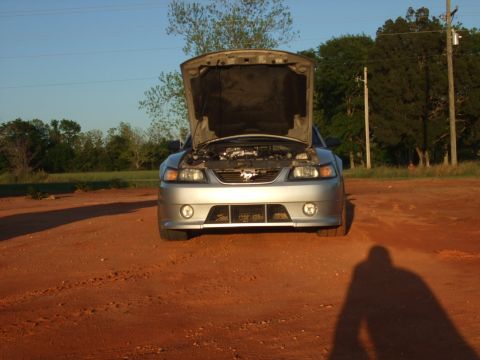 1999 Ford Mustang - Front view of a silver 1999 Ford Mustang with its hood open, parked outdoors on a dirt surface.