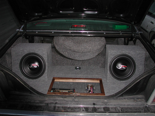 Sedan trunk with gray-carpeted custom stereo install, two subwoofers, and recessed amplifier rack