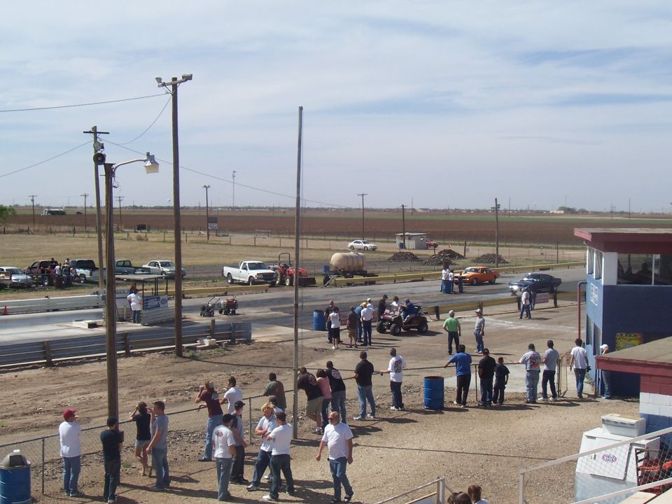 Drag strip scene with cars, ATVs, and people gathered