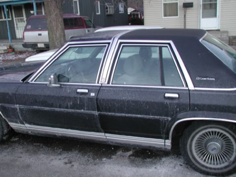 1988 Ford LTD Crown Victoria - Passenger-side profile of a dark blue Ford LTD Crown Victoria four-door sedan caked in dried road salt and grime, with chrome window surrou…