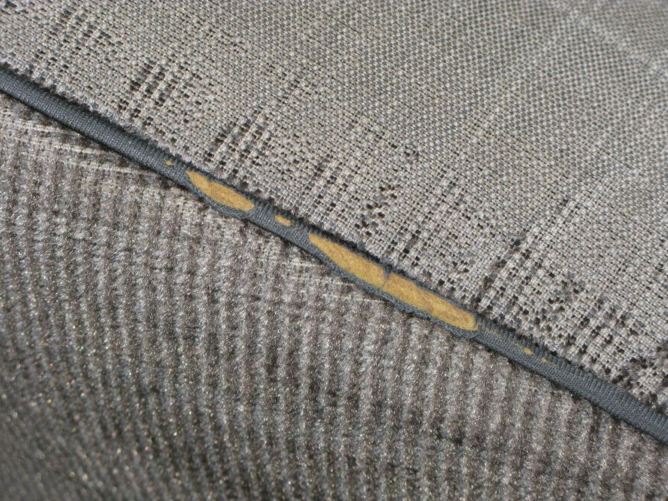 Close-up of gray fabric with a torn seam showing yellow padding underneath. Supermotors.net logo in corner