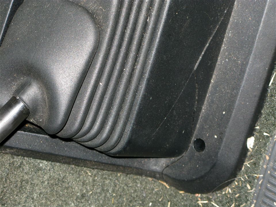 Black rubber gear shifter boot and surrounding plastic trim in a vehicle interior. Some debris is visible on the floor