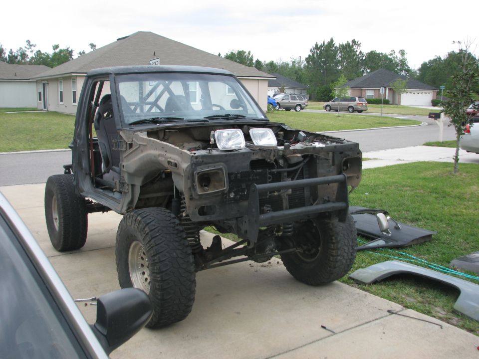 Stripped pickup body with roll cage on a driveway, front clip removed