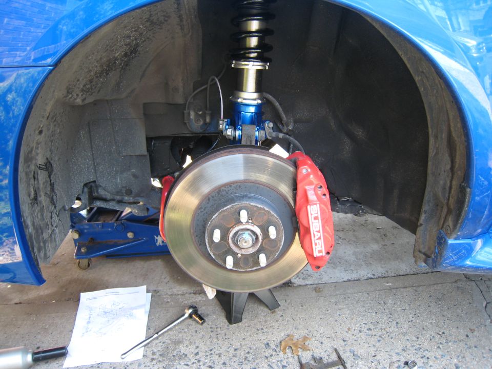 Front brake with drilled rotor, red 6-piston caliper and blue coilover on a blue car
