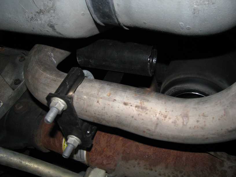 Underbody exhaust pipe held by a rubber hanger near a rusted crossmember