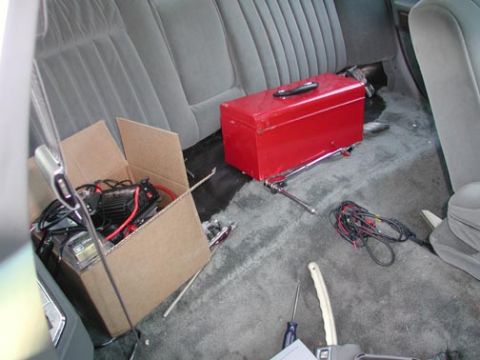 1988 Ford LTD Crown Victoria - Rear bench seat and floor of a car with gray cloth upholstery, being used as a work area during an install: a red metal toolbox sits on the…