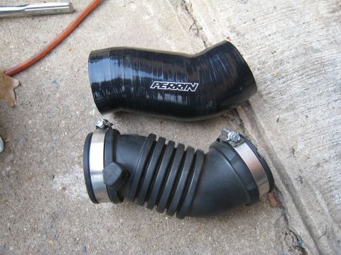 2007 Subaru Impreza - A PERRIN branded silicone intake hose and a ribbed rubber hose with metal clamps sit on a concrete surface.