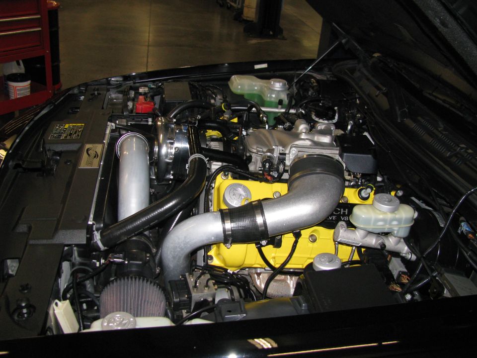 Engine bay with yellow cam covers on a 32-valve V8 and polished centrifugal supercharger piping