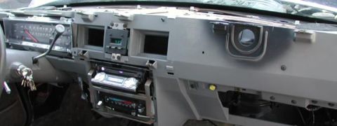 1988 Ford LTD Crown Victoria - Close-up of a bare gray dashboard frame with the woodgrain trim panels and glovebox door removed, exposing the metal structure, HVAC vent h…