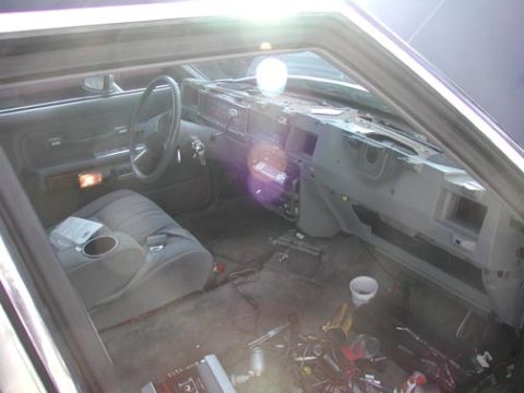 1988 Ford LTD Crown Victoria - Interior of a gutted 1980s Ford sedan shot through the open driver's door, with the dash partially disassembled, glovebox and center trim p…