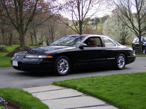 1996 Mercury Grand Marquis - A black coupe with chrome wheels is parked on a driveway, with trees and houses in the background.