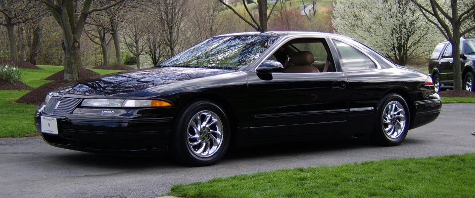 Black Lincoln Mark VIII coupe with chrome wheels parked on a driveway, three-quarter front view