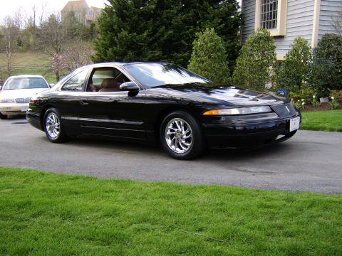 1996 Mercury Grand Marquis - A black coupe with chrome wheels is parked on a driveway in front of a house.