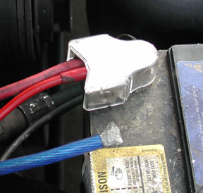 1988 Ford LTD Crown Victoria - Close-up of a car battery's positive terminal fitted with an aftermarket clear-cover distribution block, joining a heavy red power cable an…