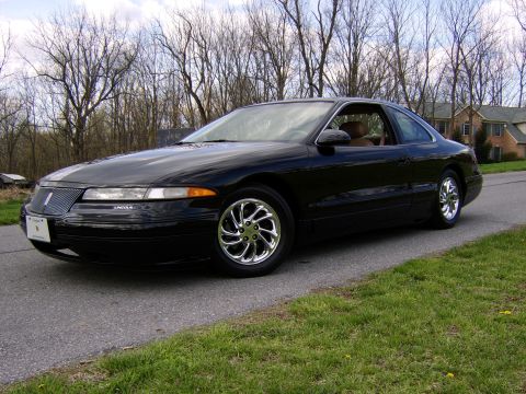 1996 Mercury Grand Marquis - A black Lincoln Mark VIII coupe is parked on the side of a road with a residential house and trees in the background.