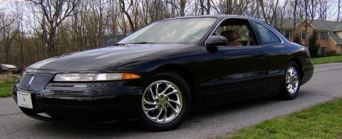 1996 Mercury Grand Marquis - A black coupe with a Lincoln badge is parked on a paved road with trees and houses in the background.