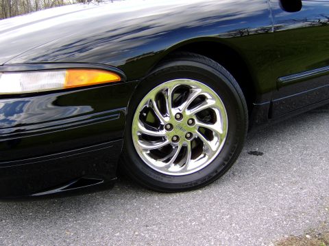 1996 Mercury Grand Marquis - Close-up of a black car's front wheel and fender, showing a chrome rim and orange turn signal.