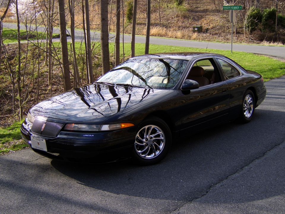 Black Lincoln Mark VIII coupe on paved drive with tree reflections on its hood