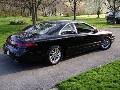 1996 Mercury Grand Marquis - A black coupe with chrome wheels is parked on an asphalt driveway, with a dark SUV visible in the background.