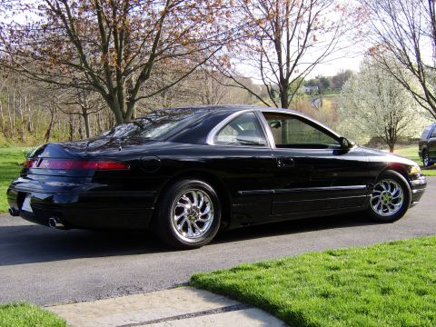 1996 Mercury Grand Marquis - This black coupe, seen from the rear quarter, features distinctive taillights and chrome wheels, suggesting it is a 1990s Lincoln Mark VIII.