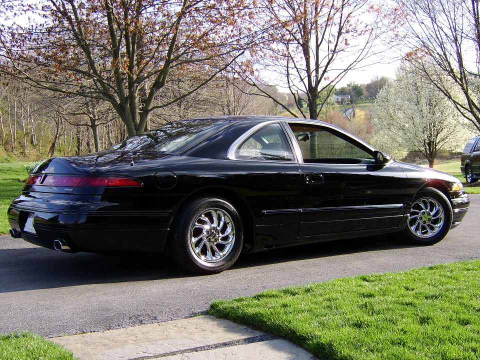 Black luxury coupe, rear 3/4 view with full-width taillight and chrome wheels