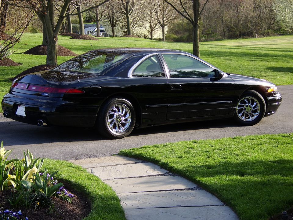 Black Lincoln Mark VIII coupe on a driveway, rear three-quarter view with chrome wheels