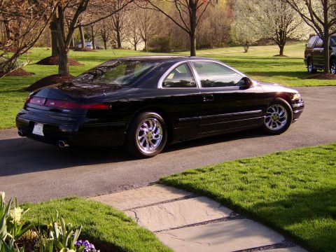 1996 Mercury Grand Marquis - A black coupe with distinctive taillights and chrome wheels is parked on a driveway, with another vehicle visible in the background.