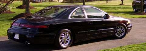 1996 Mercury Grand Marquis - A black coupe with distinctive chrome wheels is seen from the rear, parked on a driveway. Another vehicle is visible in the background.