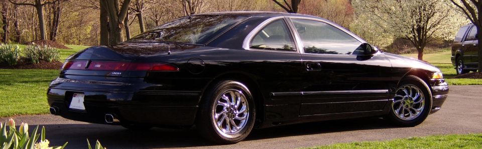 Black Lincoln Mark VIII coupe rear 3/4 view, full-width taillight and chrome wheels