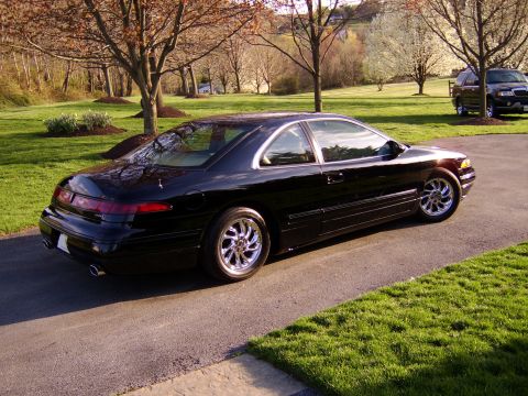 1996 Mercury Grand Marquis - A black coupe with chrome wheels is parked on an asphalt driveway with a grassy lawn and trees in the background.