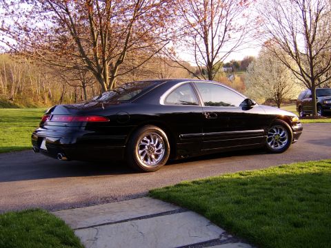 1996 Mercury Grand Marquis - A black coupe with distinctive taillights and chrome wheels is parked on a driveway, with a second vehicle visible in the background.